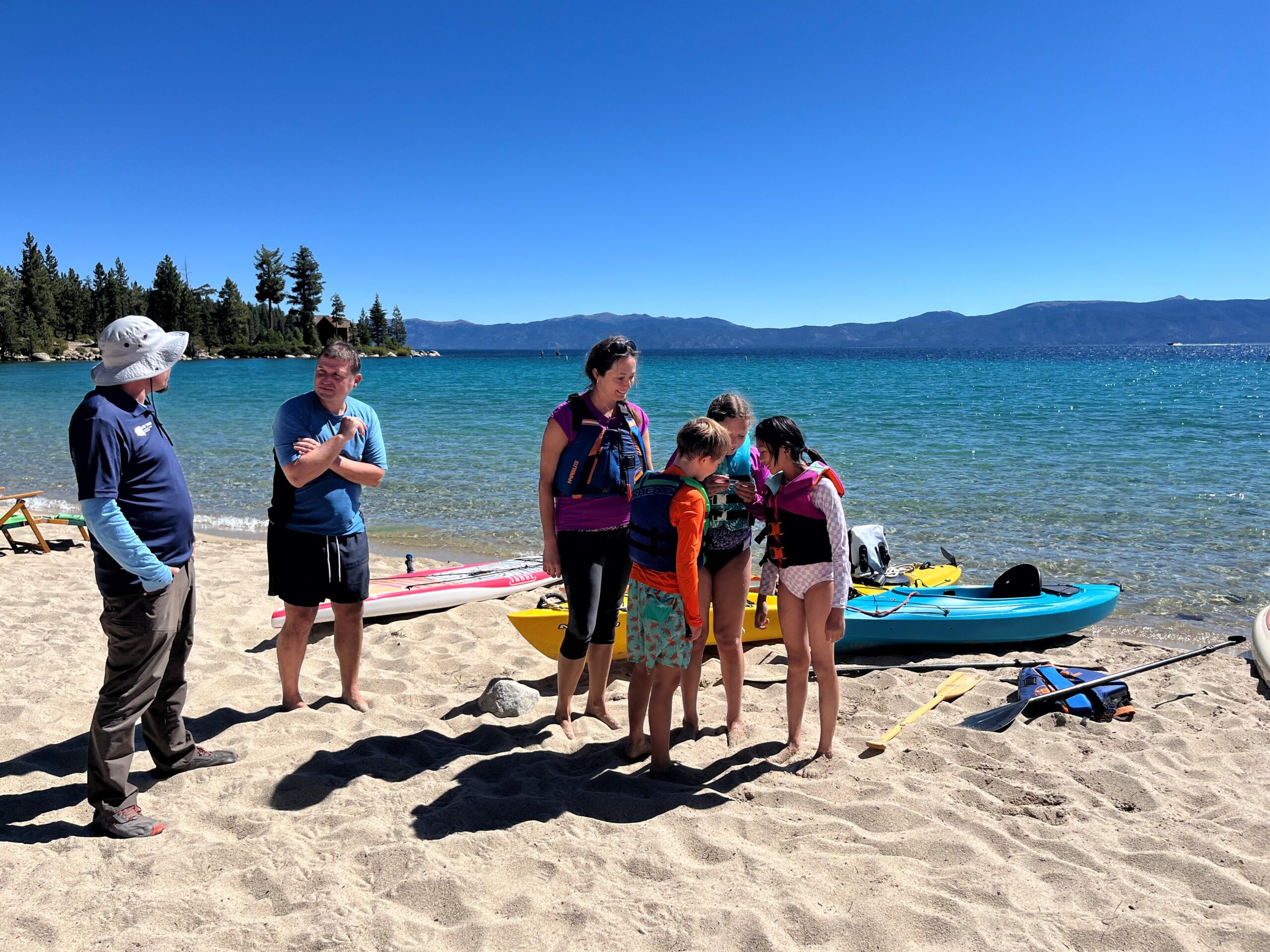 Roving inspector talks with a family of kayakers on the beach in Lake Tahoe.